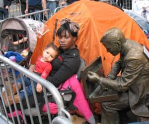A bronze statue of a Wall Street trader leans toward a jobless mother and her child at Occupy Wall Street.
